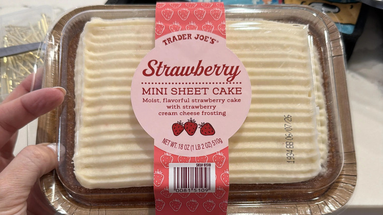 Someone holds a container of Trader Joe's Strawberry Mini Sheet Cake