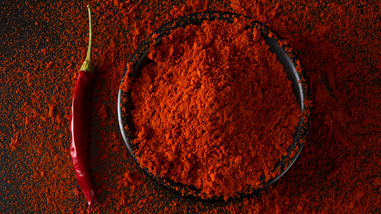 Paprika overflowing from a bowl onto a table with a pepper