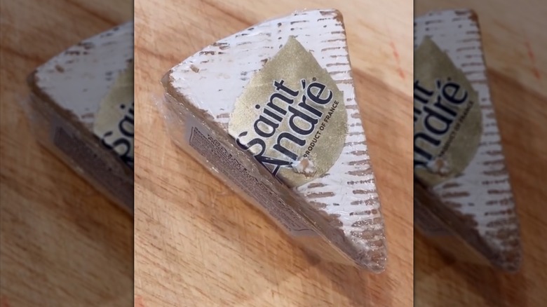 Saint André Triple Crème Brie in packaging on wood cutting board.