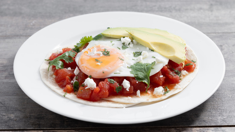 huevos rancheros on a white plate on a wooden table