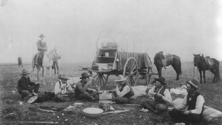 historical image of cowboys eating on the range with a chuckwagon in the background