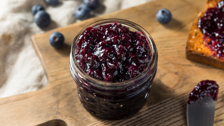 Blueberry jam in a glass jar on a wooden board.