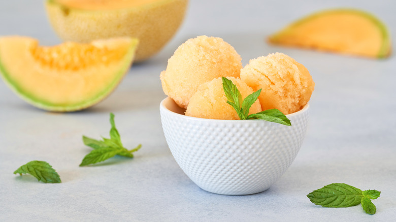 frozen cantelope ice-cream in a white bowl with slices of the fruit in the background