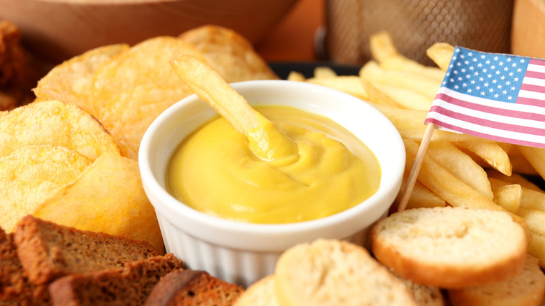 small dish of mustard dip with french fry in it and food around it