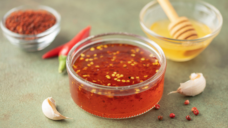 a glass jar of hot honey, with garlic cloves and peppercorn in the foreground and a bowl of honey in the background