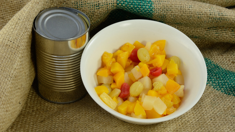 Fruit cocktail next to open can on burlap
