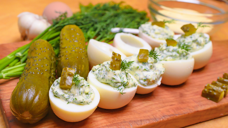 Deviled eggs on a cutting board with pickles and herbs