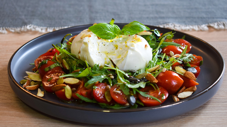 A mound of burrata cheese oozes on a plate of salad