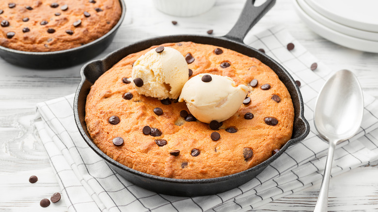Cookie skillet in cast iron pan, chocolate chips and ice cream on top next to spoon.