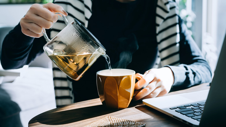 Woman pouring tea into a cup from pitcher