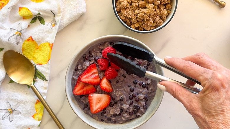 hand adding raspberry to bowl of blueberry oats