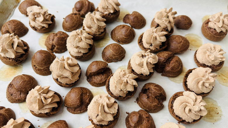 Chocolate pastries on baking sheet with half topped with cream swirls