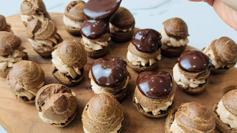 Cream puffs on wooden board with some topped with chocolate ganache