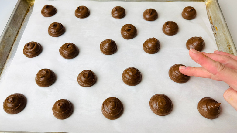 Hand touching top of chocolate dough mound on baking sheet