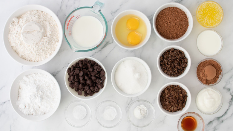 Dry ingredients and wet ingredients for chocolate baked donuts with cereal toppings laid out on marble surface