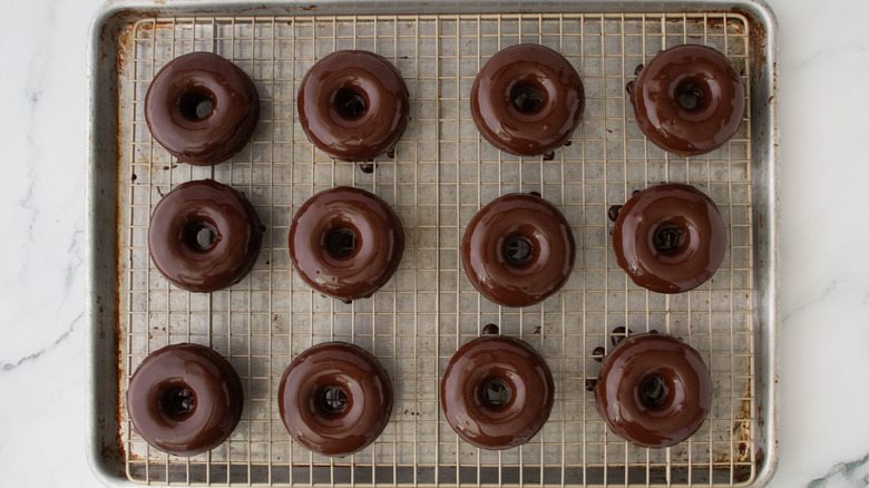 Glazed chocolate donuts on wire rack over baking sheet