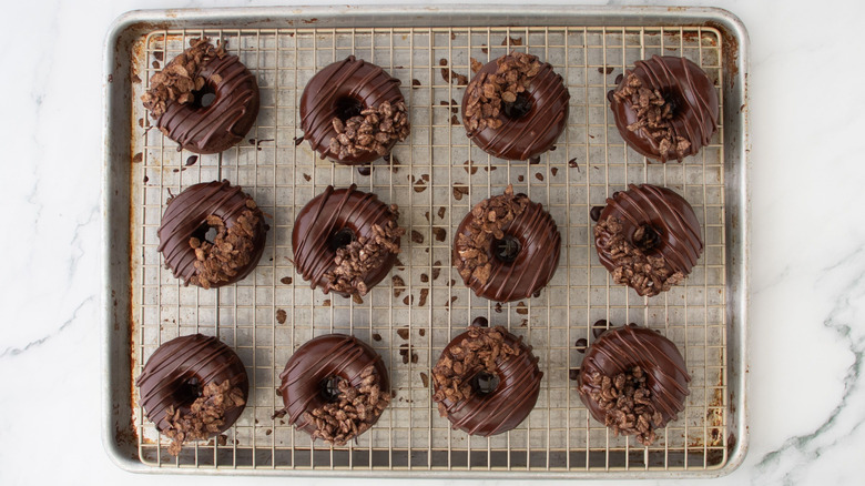 Decorated chocolate donuts on wire rack over baking sheet
