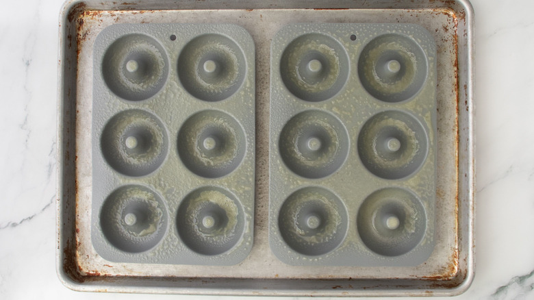 Two donut molds sprayed with cooking spray sitting on baking sheet