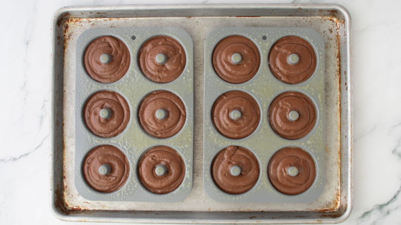 Chocolate donut batter in donut molds sprayed with cooking spray