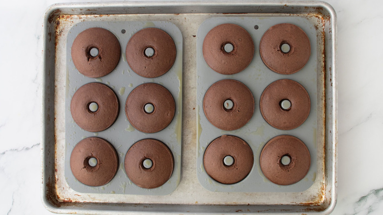 Baked chocolate donuts in donut molds on top of a baking sheet
