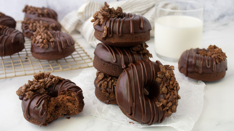 Cereal-topped chocolate donuts stacked on parchment paper with small glass of milk in the back