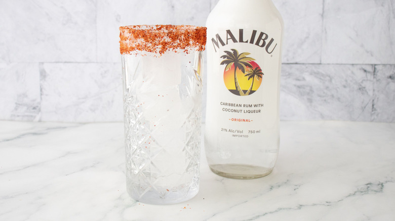 Tajín-rimmed glass in front of Malibu rum bottle