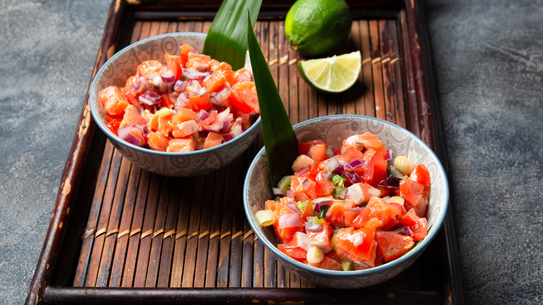 Two bowls of lomi lomi salmon served with limes on the side