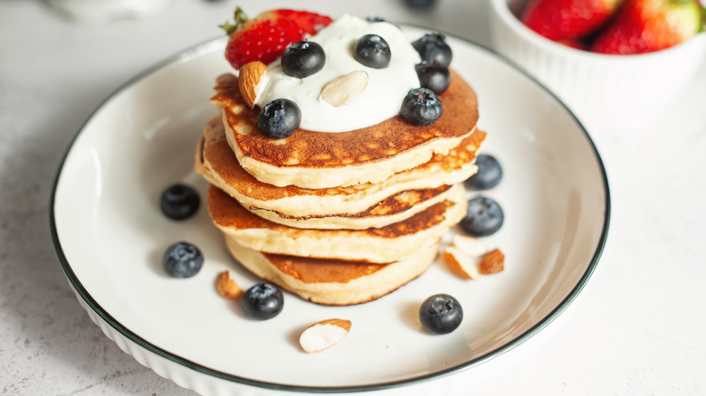 Four fluffy pancakes topped with fruit and cream.