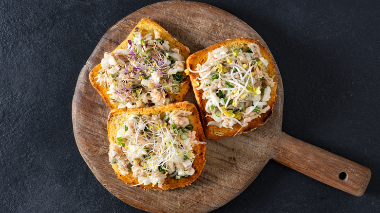 Three pieces of toast with tuna salad on a cutting board