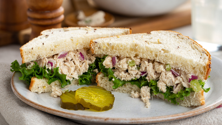 Two halves of a tuna sandwich on a plate with two pickles