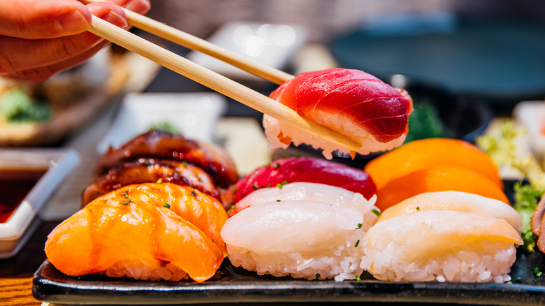 A plate of sushi with one being picked up with chopsticks