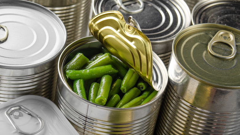 Can of opened green beans in the middle of various other unopened cans.