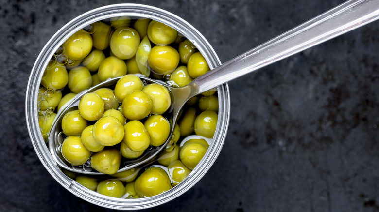 a spoon dipping into an open can of peas