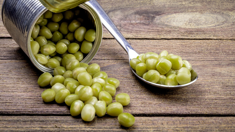 An open can of peas is styled on a wooden table.