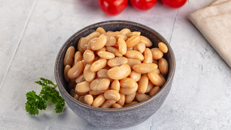 A bowl of white cannellini beans, with a sprig of parsley on the side.