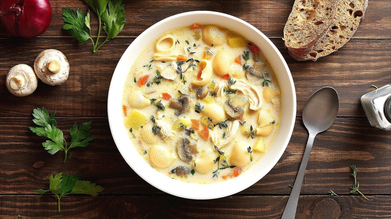 Bowl of creamy chicken soup with cooked pasta on a wooden table