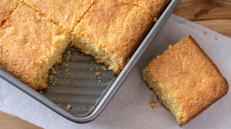 A pan of cornbread squares with one removed to parchment.