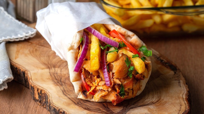 Chicken gyro with sliced red onion and red pepper, fries, and cilantro wrapped in butcher paper