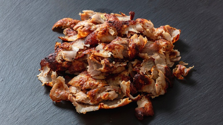 Pile of thin, gyro-style chicken on a black matte surface