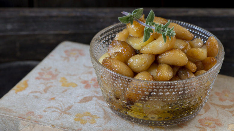 Garlic confit in glass dish with a sprig of green herb on top