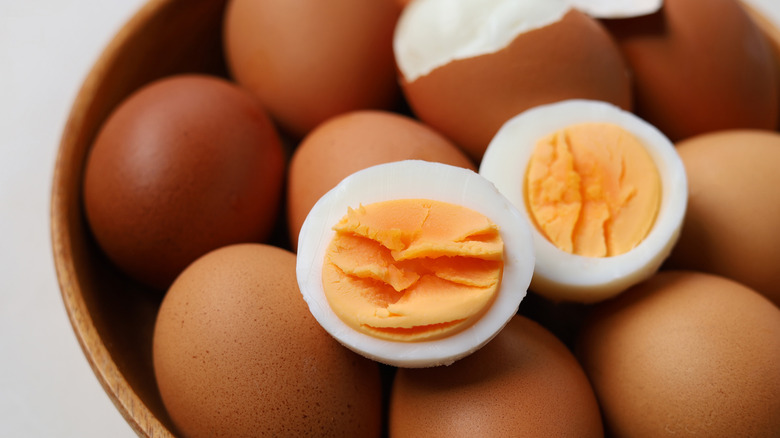 A sliced hard-boiled egg sitting on top of a bowl of unpeeled eggs