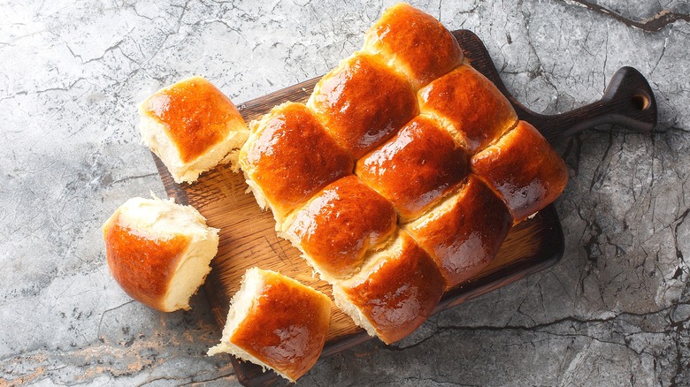 Homemade batch of Hawaiian sweet rolls on a wooden serving board on a marble gray surface