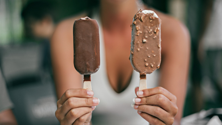A person holds two chocolate-covered popsicles