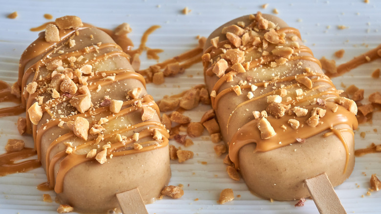 Peanut butter popsicles in a row with crushed peanuts.