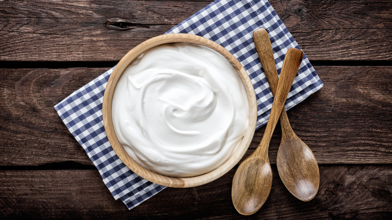 Bowl of sour cream on a checkered cloth sitting beside two wooden spoons