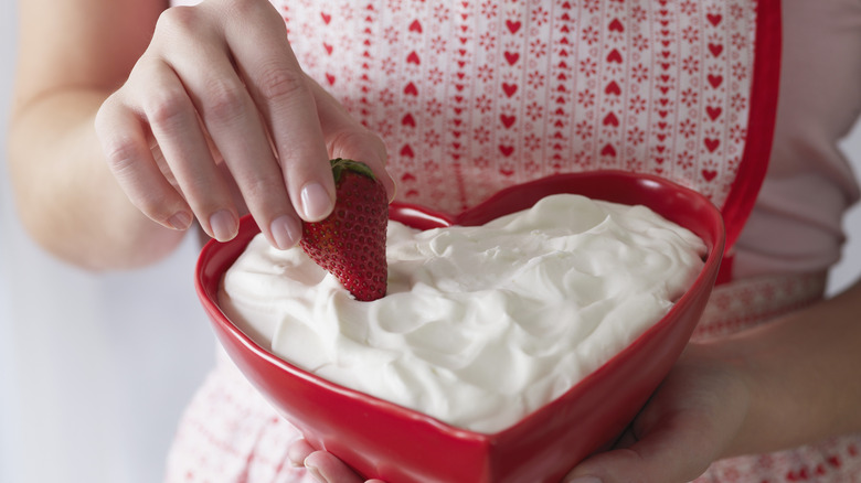 A hand dipping a strawberry into a white dairy-based dip