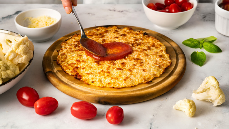 Person adding sauce to pizza crust