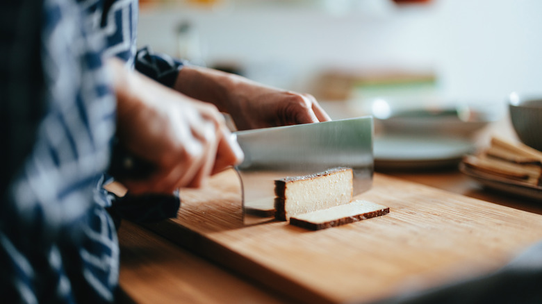 Person slicing tofu on cutting board