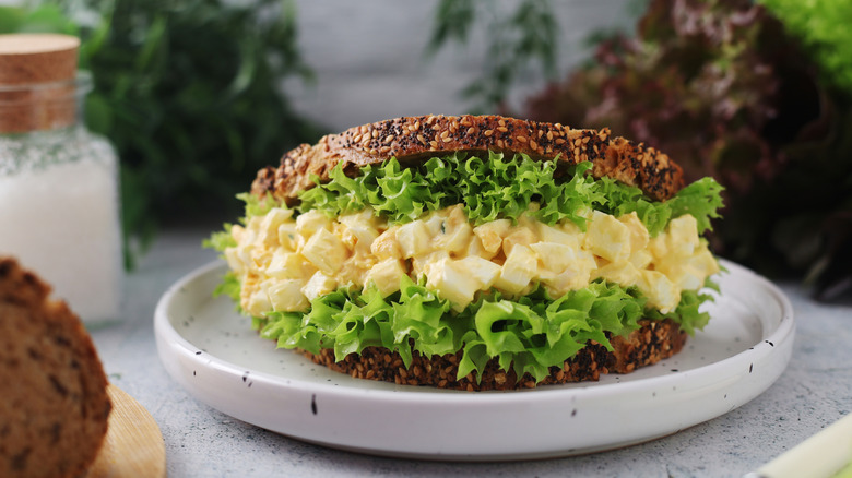 Creamy eggs nestled in grainy bread and lettuce served on a white plate