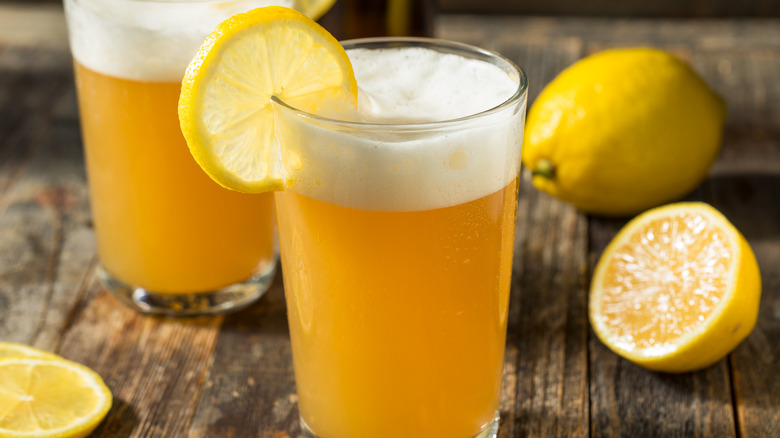 Shandy with a lemon garnish beside halved and whole lemons
